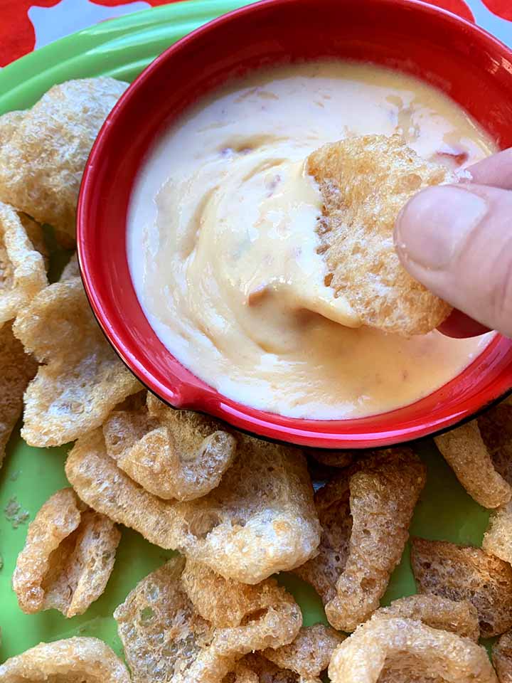 a hand dips a pork ring into a small bowl of low carb cheese sauce