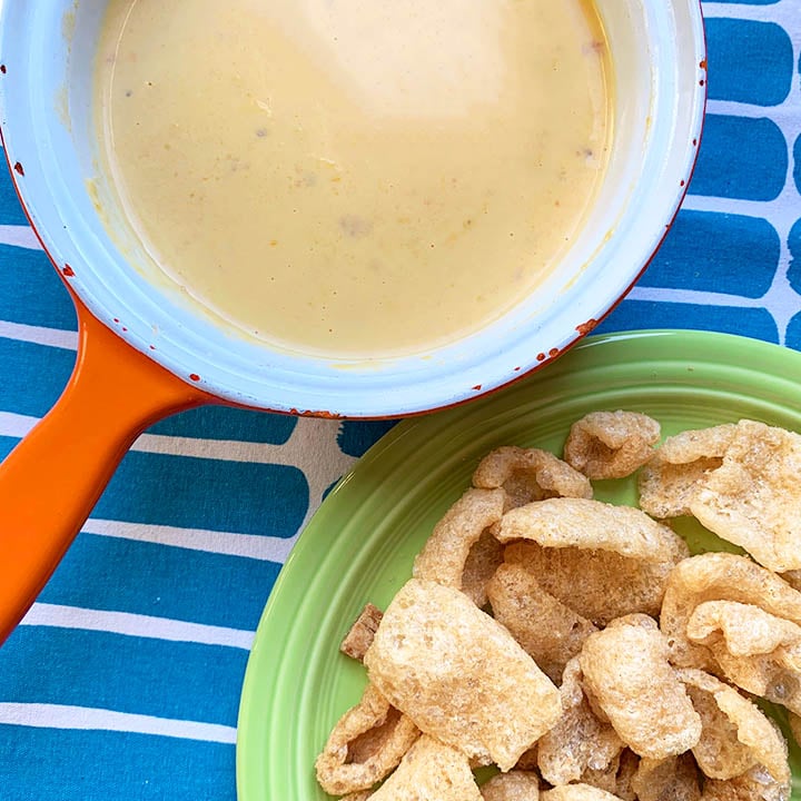 a top down view of a sauce pan filled with gluten free Mexican cheese sauce beside a green bowl of pork rinds