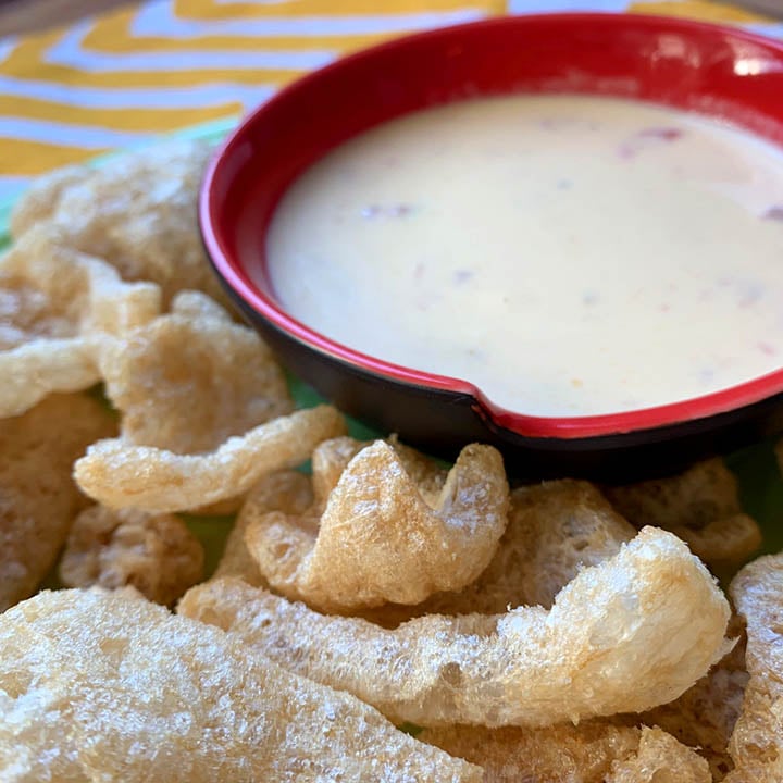 a red bowl holds keto cheese sauce and is surrounded by zero carb pork rinds