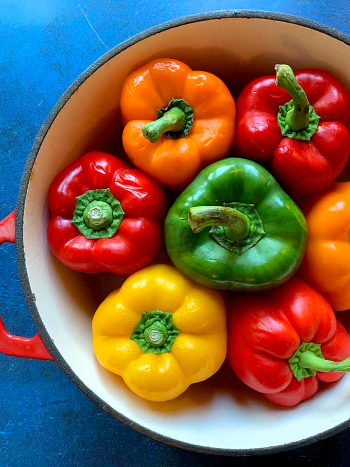 a dutch oven filled with fresh green, yellow, orange and red bell peppers