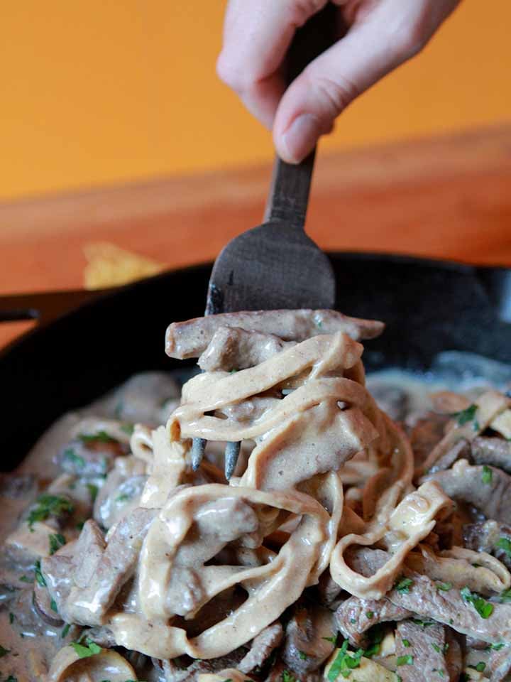 a hand twirls some egg noodles on a large fork