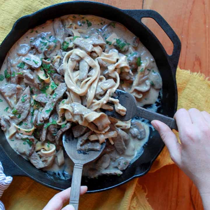 two hands scoop up some low carb Beef Stroganoff