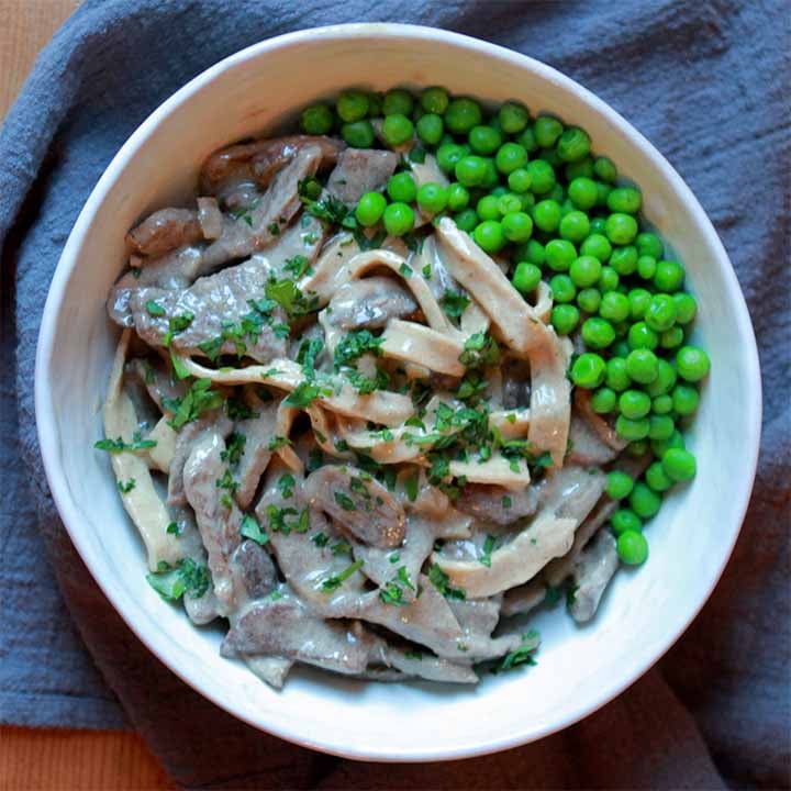 a white bowl holds Low Carb Keto Beef Stroganoff garnished with peas
