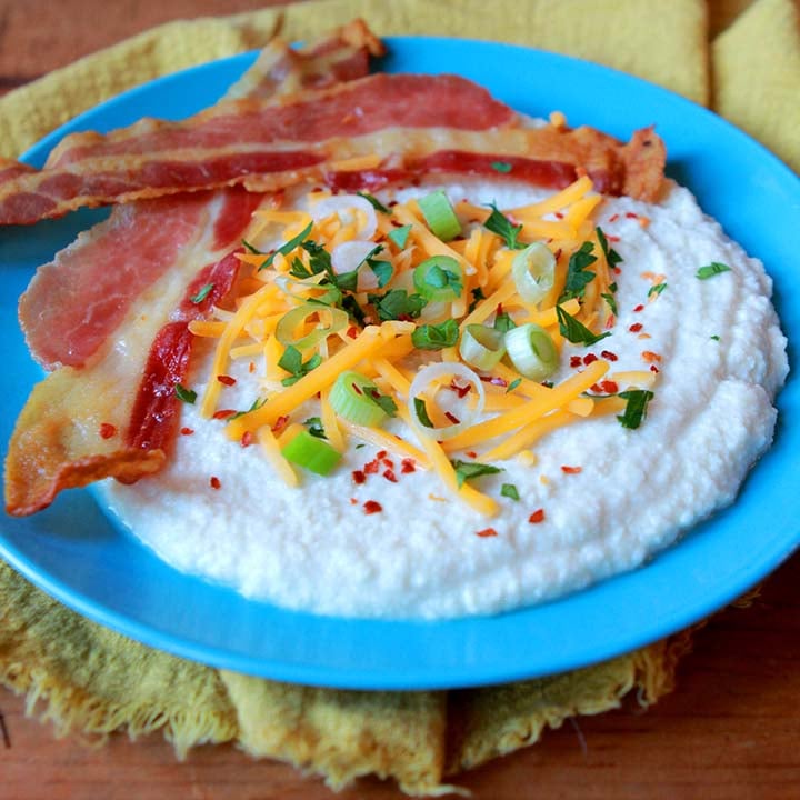 a blue plate with keto cheese grits, bacon and toppings