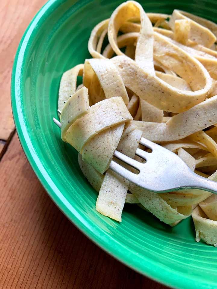 a close up of a forkful of quick low carb noodles in a green bowl