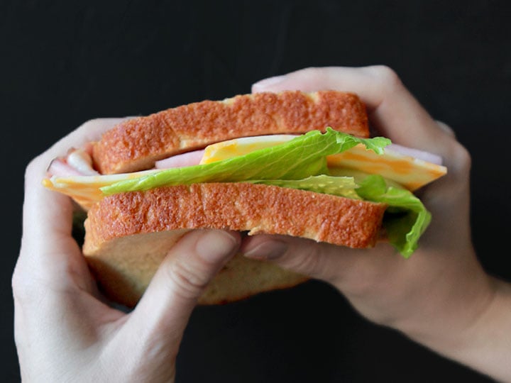 two hands hold a low carb sandwich made from a Keto bread recipe with yeast.