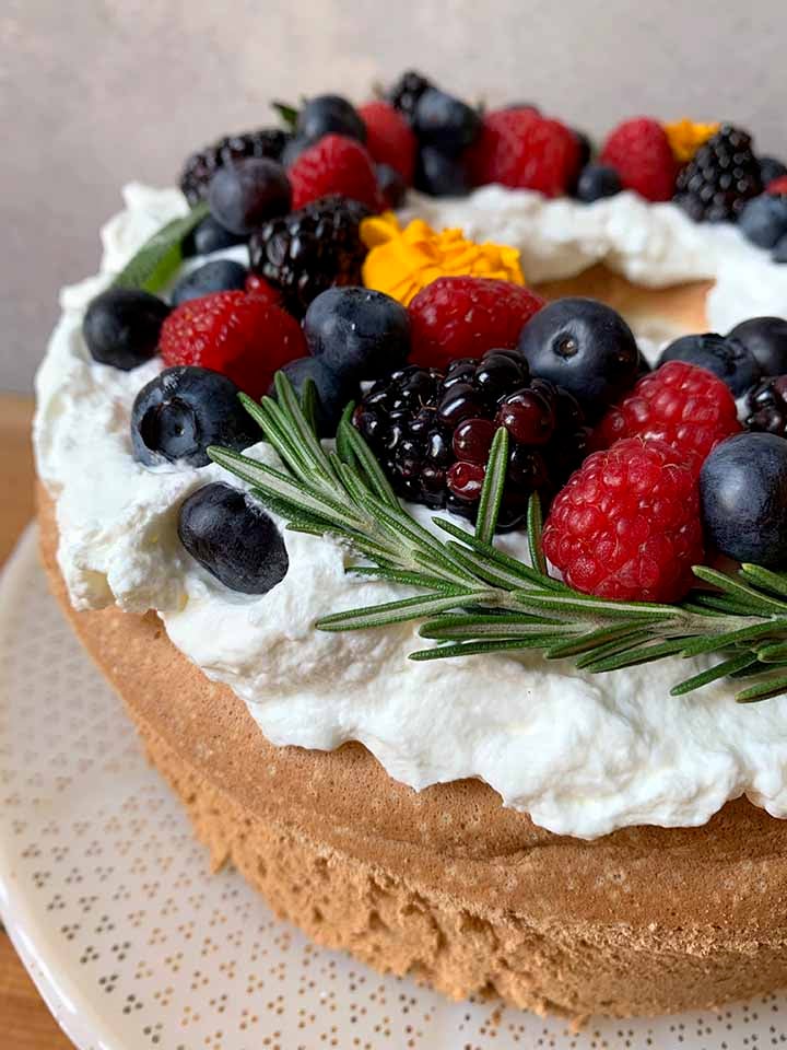 a low carb sponge cake with a wreath of berries and fresh herbs on top