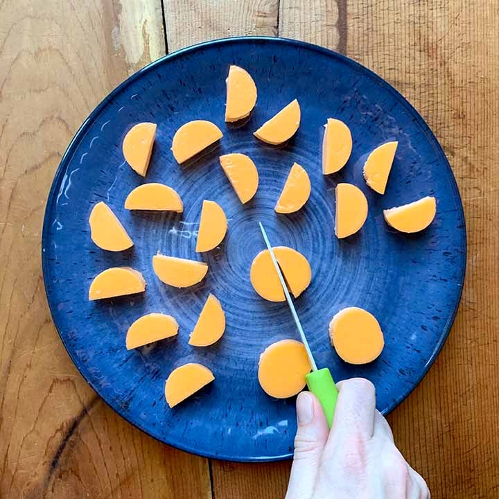 a hand cuts a circle of orange Jello in half with a knife