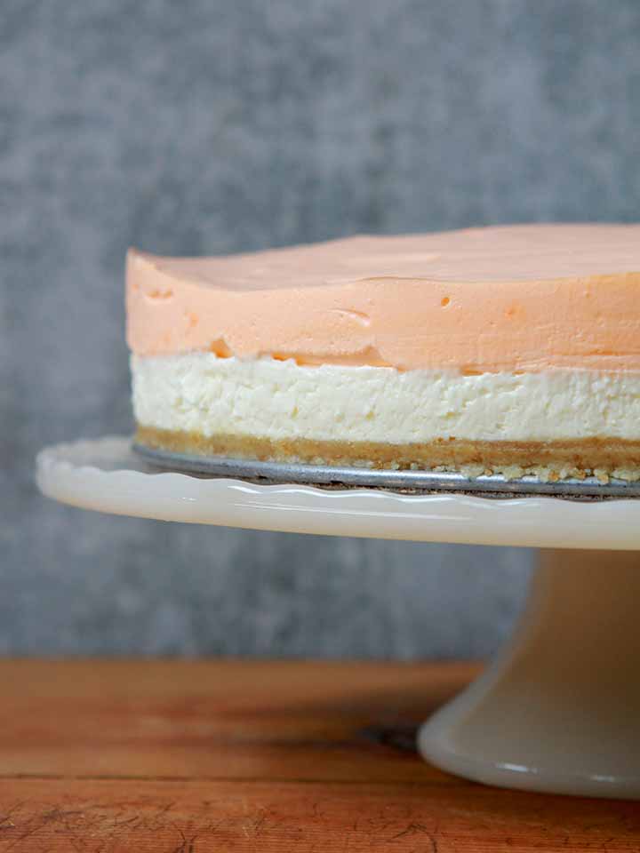 a Keto layered orange creamsicle cheesecake on a pedestal