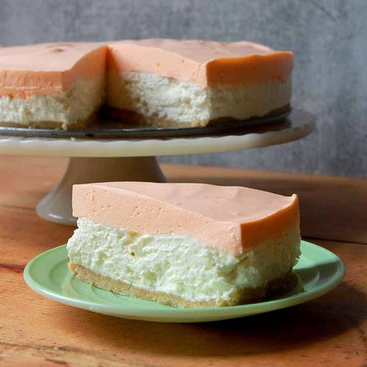 a slice cheesecake in front of the rest of the cheesecake on a pedestal