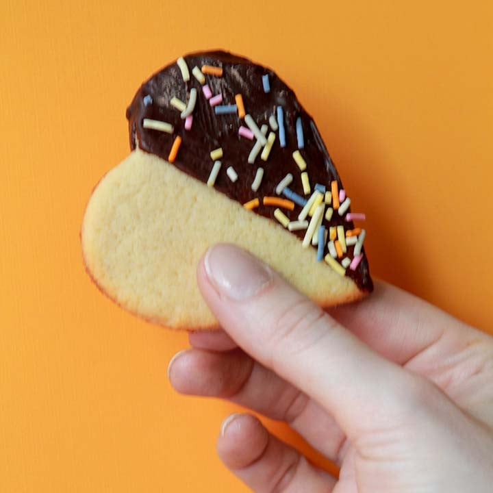 a hand holds a sugar-free heart cookie against a yellow background