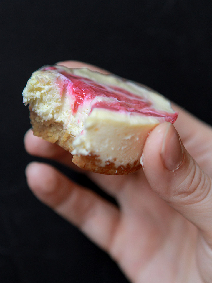 a hand holds a Keto mini cheesecake against a black background