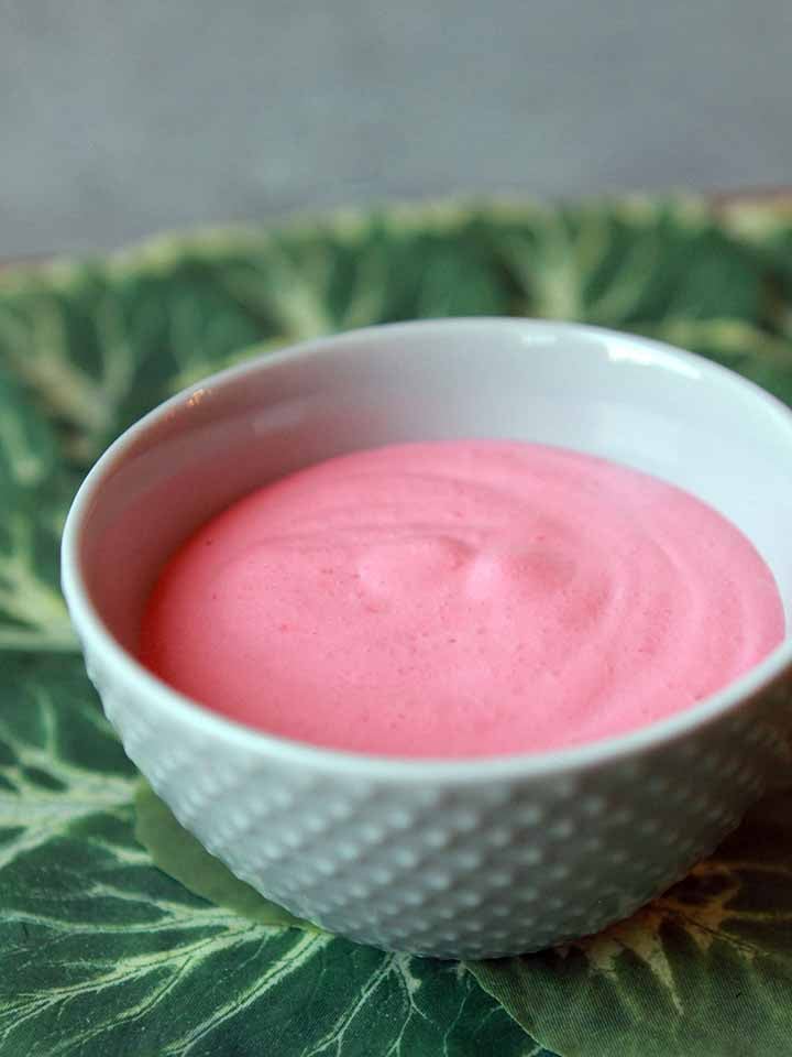 a bowl full of raspberry Jello whip against a green leafy background