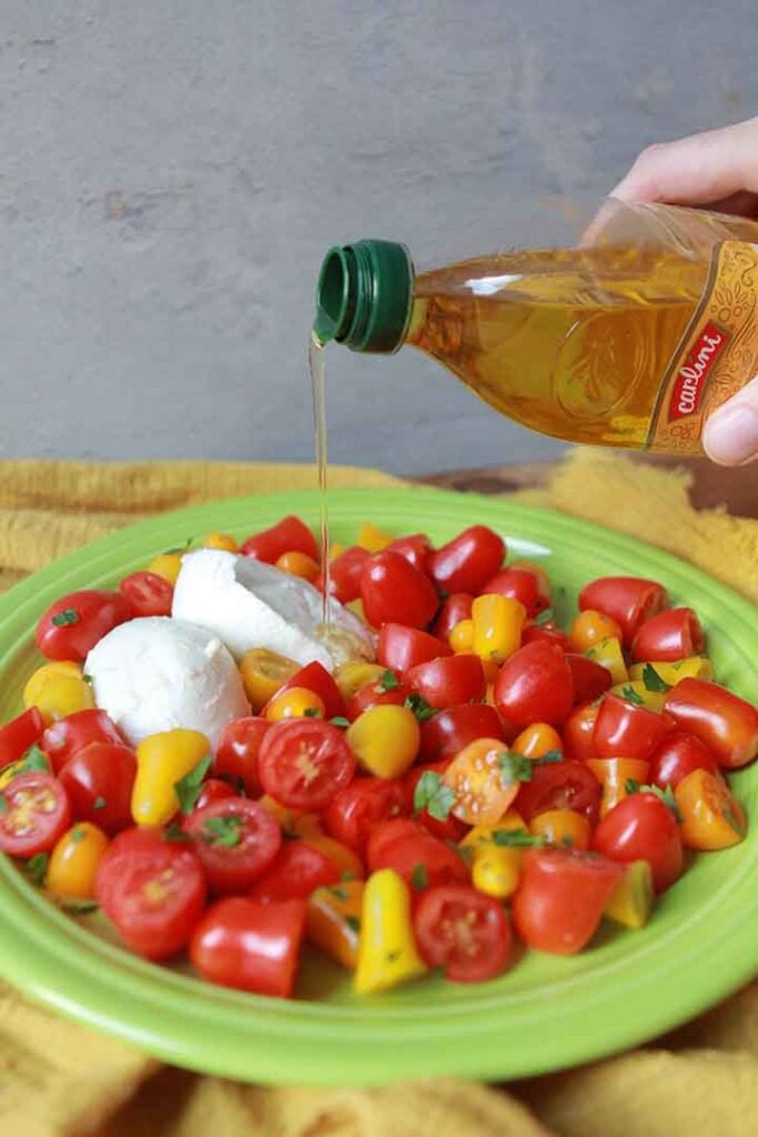 a hand pours olive oil onto a tomato and mozzarella salad