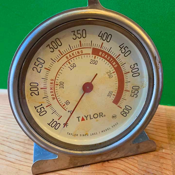 an oven thermometer against a green background