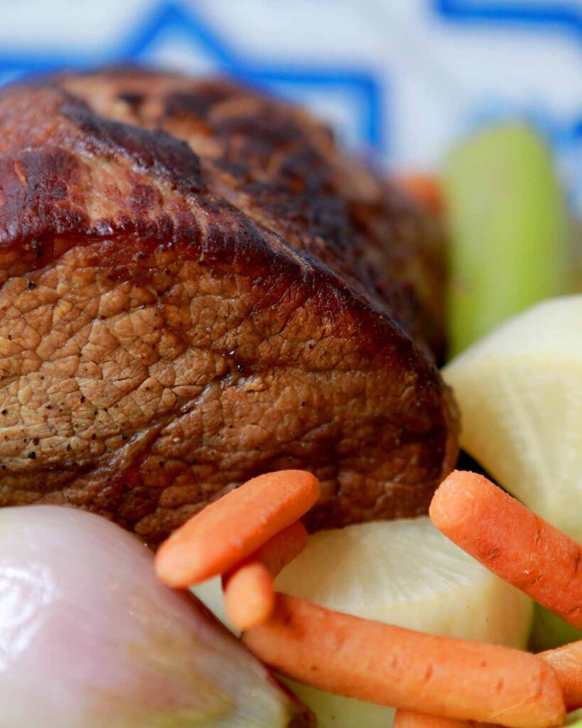 a close up on a roast of beef with carrots, onions and daikon radishes