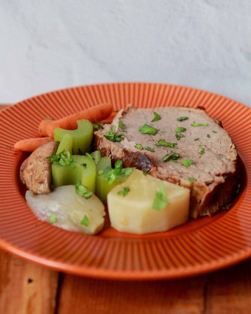 a slice of meat with daikon radishes, celery and carrots on an orange plate