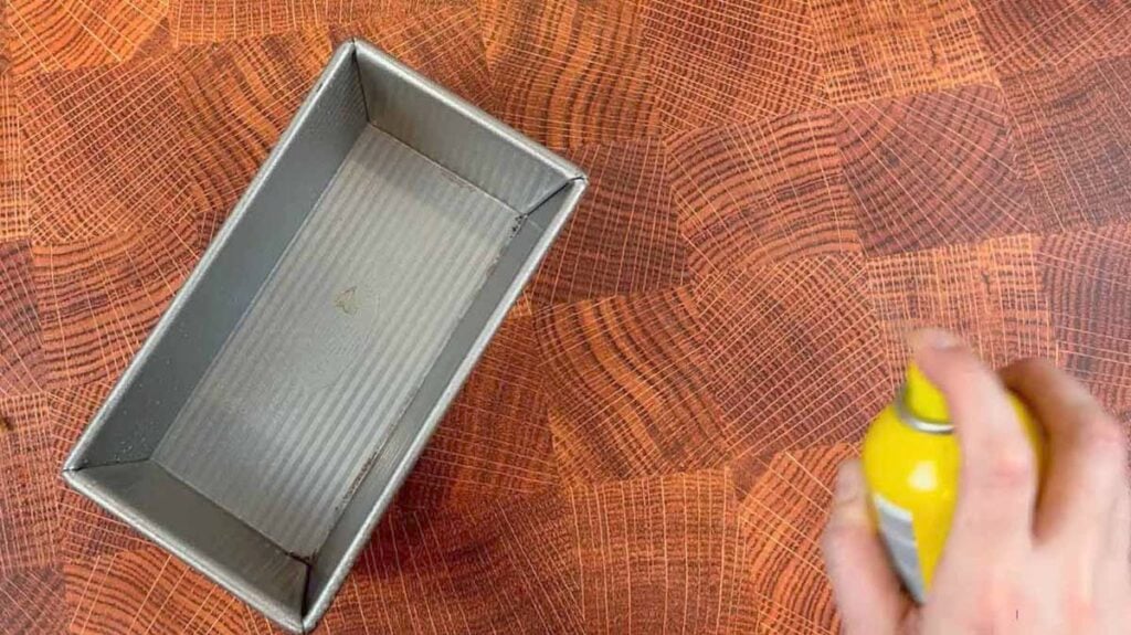 a hand sprays a loaf pan with cooking spray