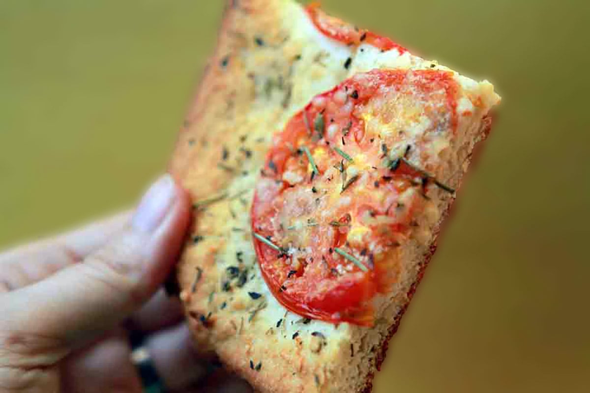 A hand holds a slice of Carbquick Focaccia.